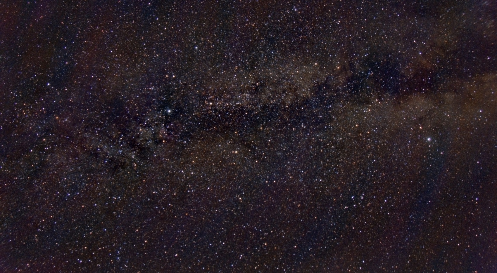 A dense band of the Milky Way running across the frame, split lengthways by a dark lane of dust, with thousands of stars and pale star clouds either side